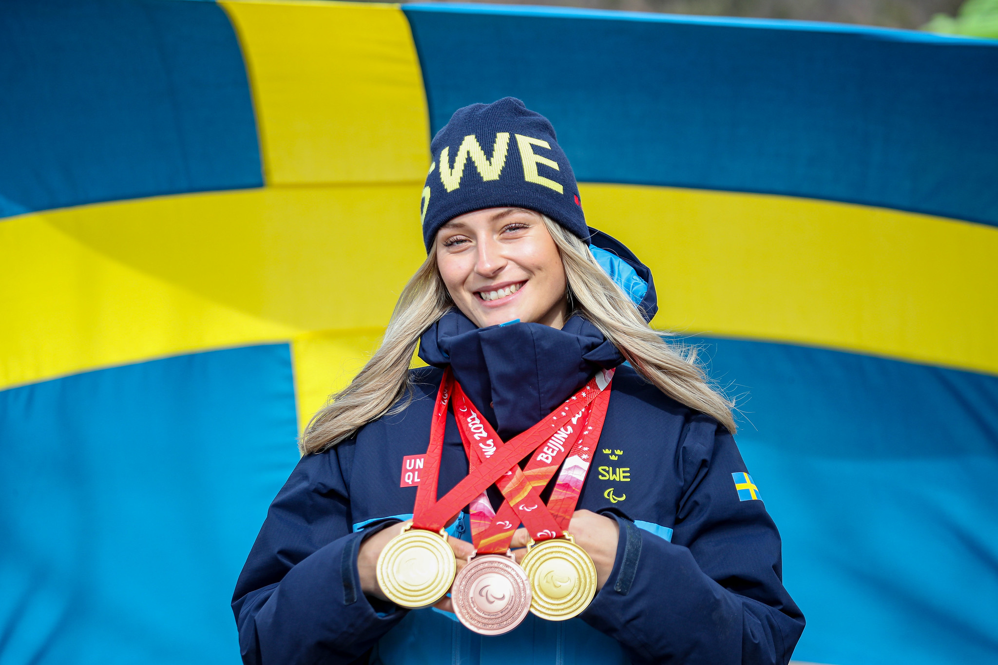 Ebba Årsjö framför svenska flaggan med sina medaljer från Peking.